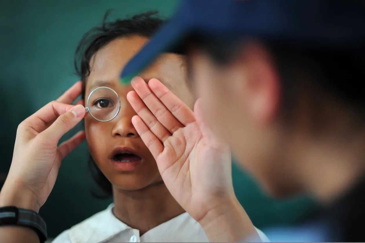 Young girl looking through a trial lens frame to determine her glasses prescription at a community eye check