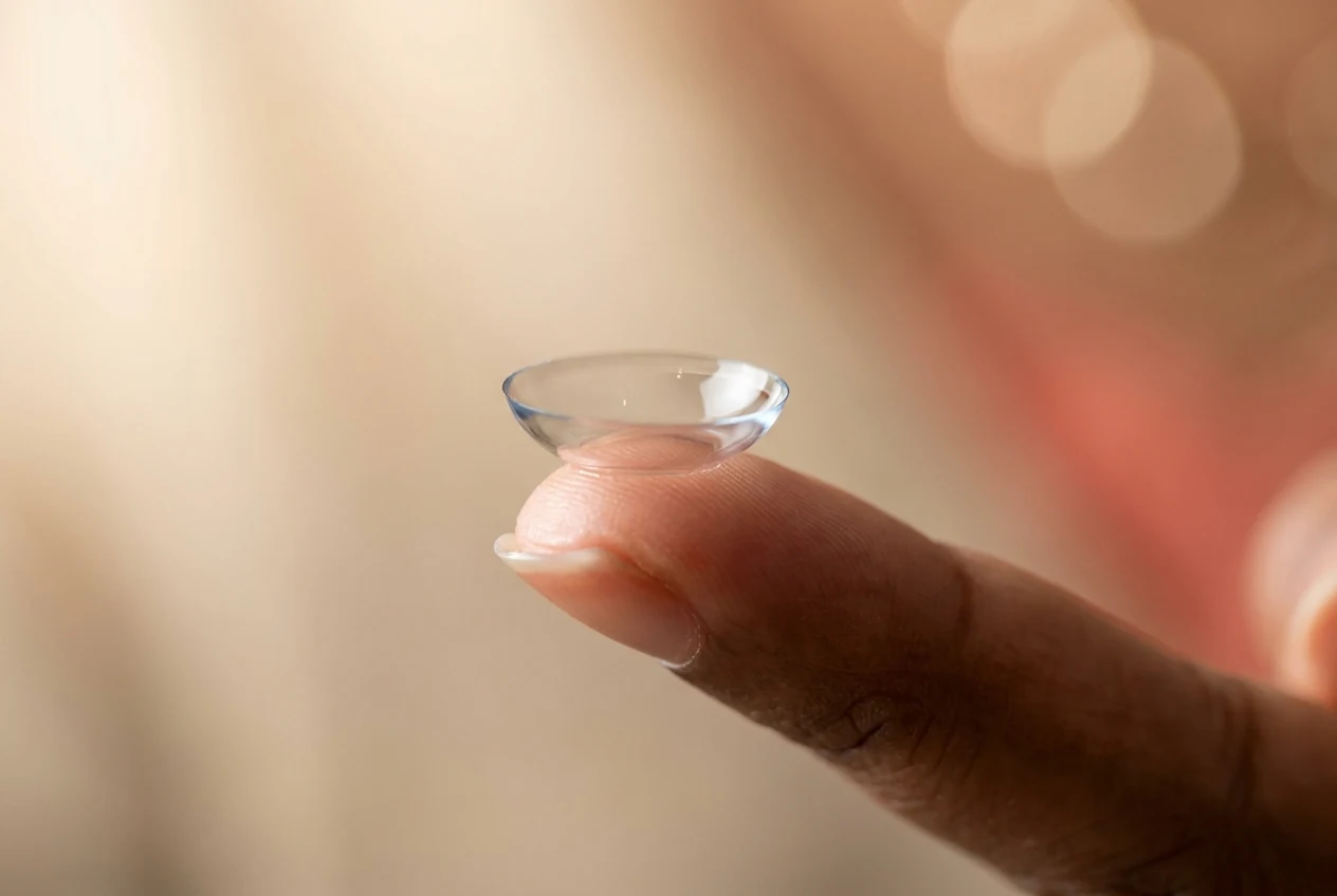 A close-up of a contact lens being placed on a fingertip, illustrating contact lens care and fitting.