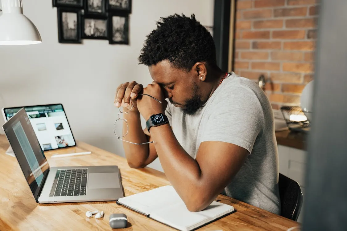 Man rubbing tired eyes while sitting at laptop showing digital eye strain symptoms