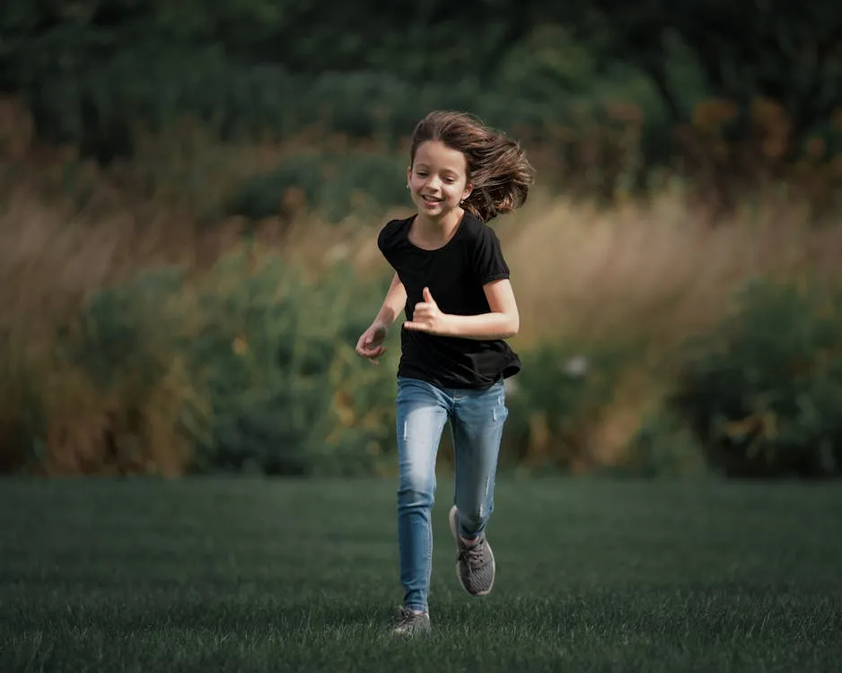 Child running joyfully through a sunny green field — outdoor time reduces myopia onset risk in children