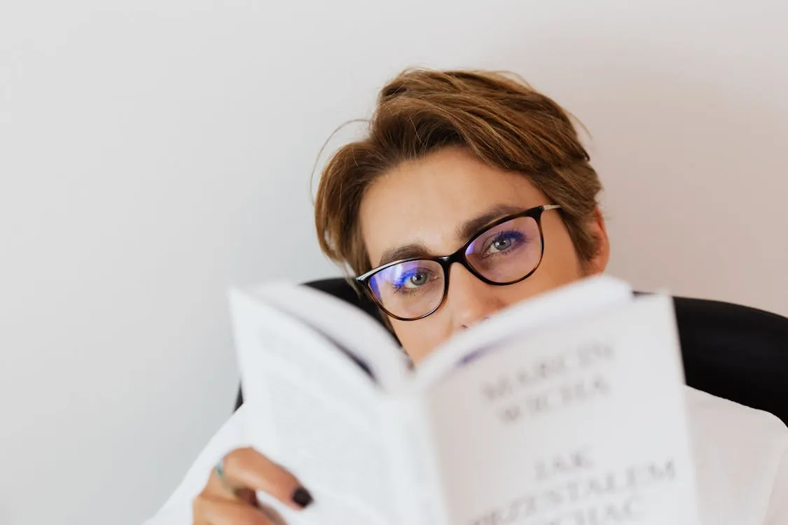 Woman wearing eyeglasses reading a book comfortably at home, demonstrating progressive lens near vision correction